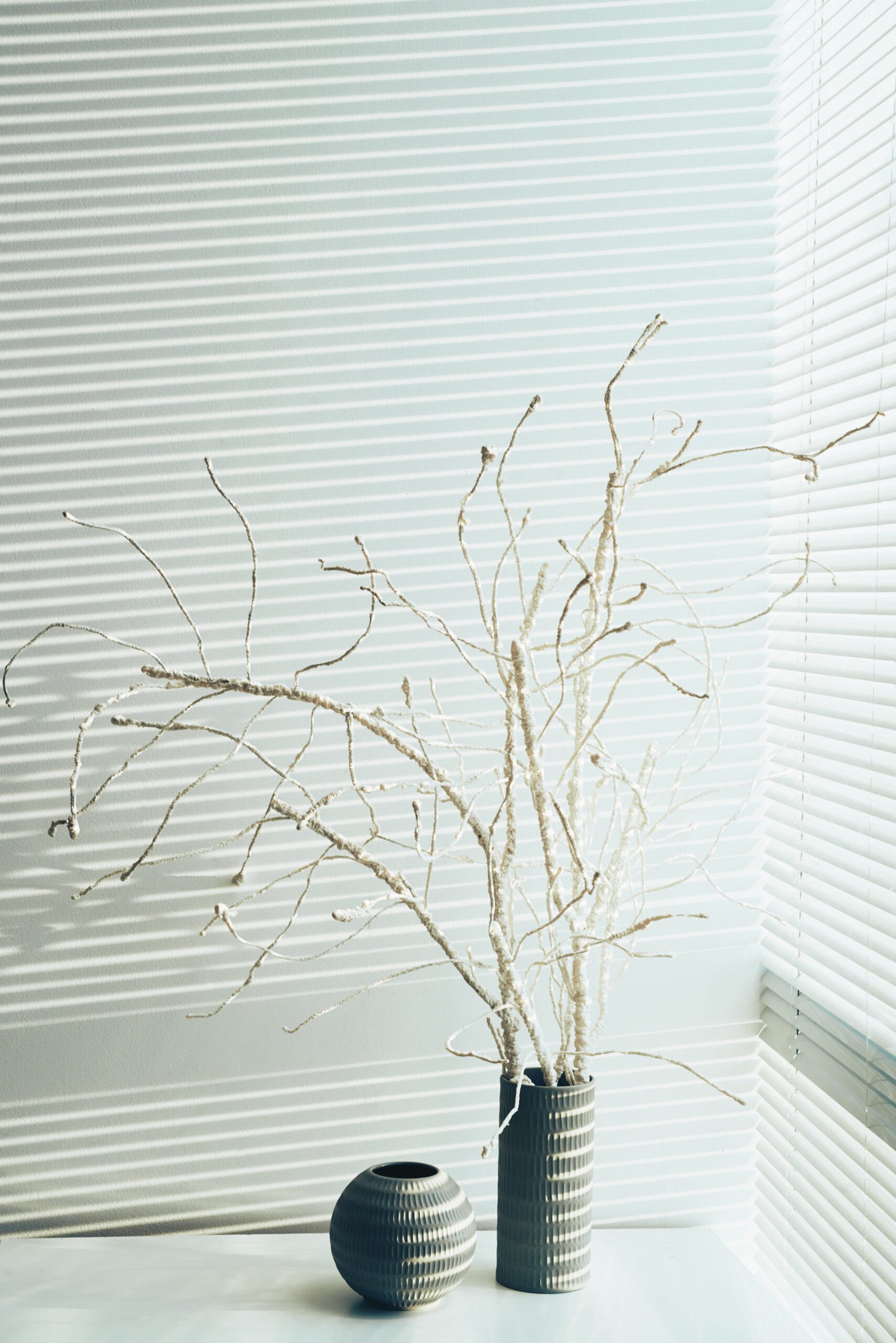 Two vases on table near window with blinds